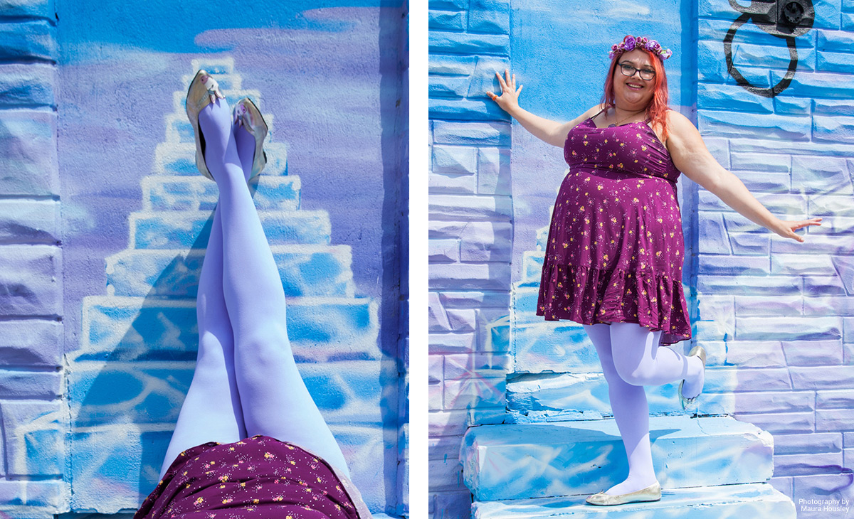 Plus size woman wearing floral print dress and lilac tights standing against a lilac wall