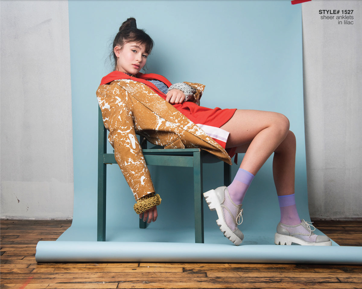 Girl stting on a chair with a blue backdrop wearing colored clothes