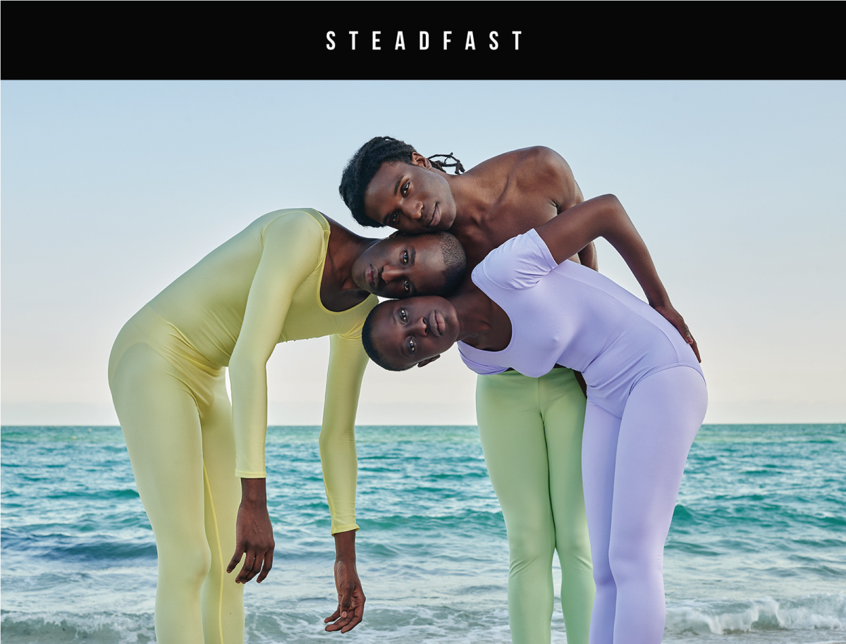 three people standing together wearing unitards and performance tights in pastel colors with ocean in the back